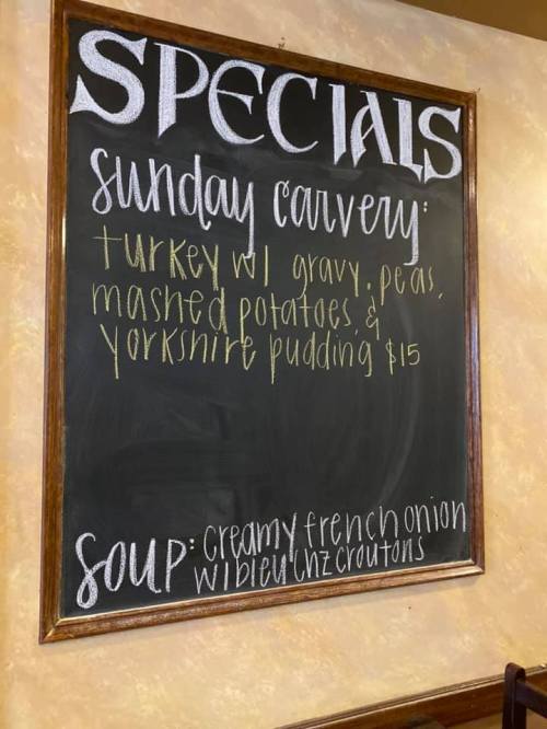 Chalkboard menu listing Sunday carvery specials: turkey with gravy, peas, mashed potatoes, Yorkshire pudding, and soup.