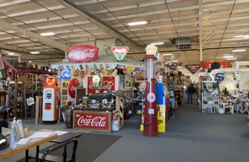 A vintage shop filled with Coca-Cola memorabilia, antique signs, and collectibles in a spacious, well-lit interior.