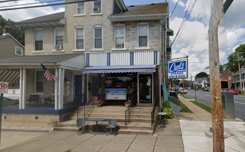A storefront of Carl's Corner, featuring a sign for steaks and subs, with outdoor seating and an American flag.