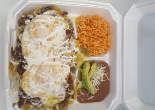 A takeout container with nachos topped with eggs, rice, refried beans, avocado, and drizzled with sauce.