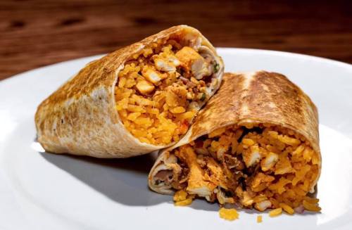 Two burritos filled with rice and chicken, cut in half, resting on a white plate.