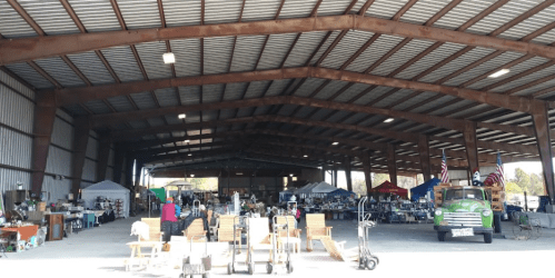 A spacious indoor market with various items for sale, including furniture and decorations, under a metal roof.
