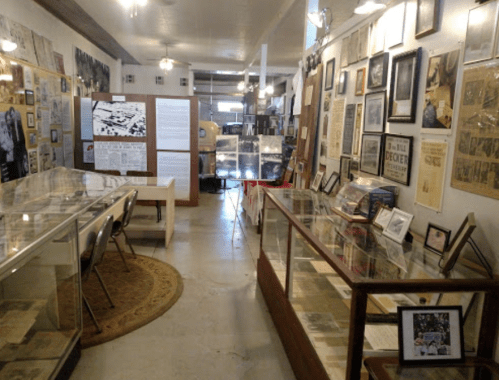 A museum interior featuring display cases, historical documents, and photographs on the walls.