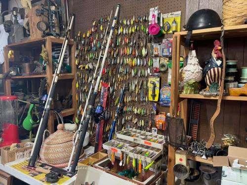 A cluttered display of fishing gear, including rods, lures, and various antique items on shelves and tables.