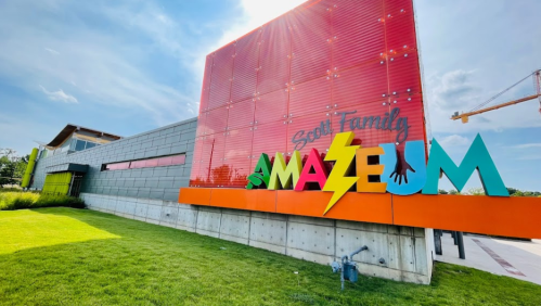 Colorful exterior of the Scott Family Amazeum, featuring bold signage and a grassy area under a bright sky.