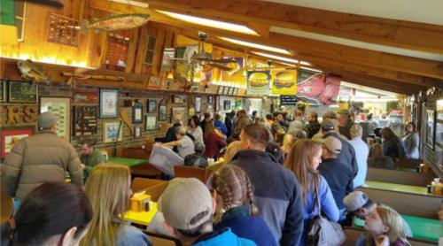 A crowded restaurant interior with people seated and standing, wooden decor, and various food-related memorabilia on the walls.