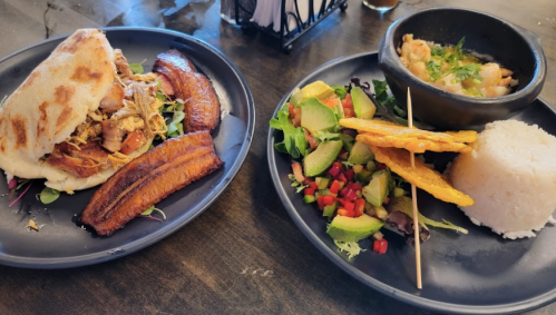 A plate featuring a stuffed arepa, fried plantains, salad, rice, and a bowl of shrimp soup.