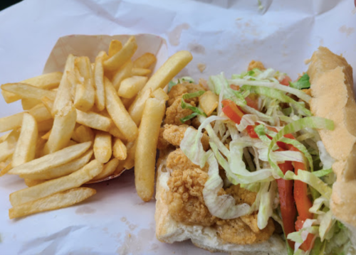 A sandwich filled with fried chicken, lettuce, and tomatoes, served with a side of golden French fries.