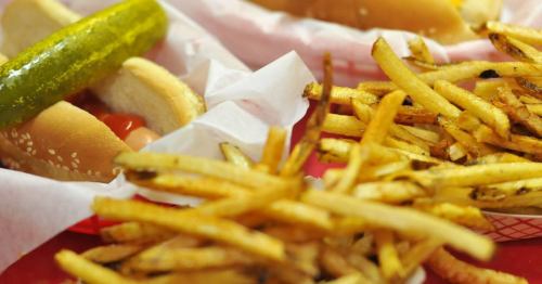 A close-up of hot dogs with pickles and a side of golden French fries on a red tray.