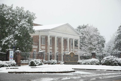 Historic building covered in snow, surrounded by trees and a snow-blanketed landscape. Winter scene.