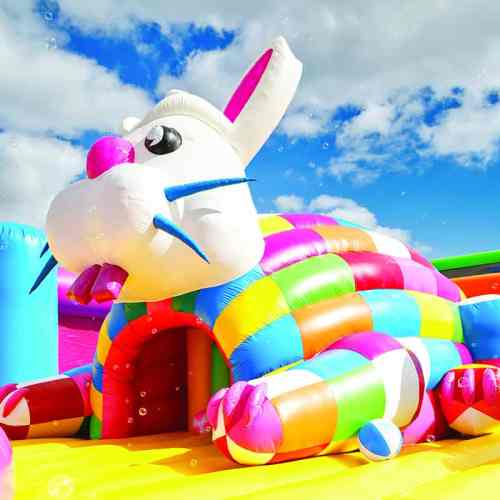 A colorful inflatable bunny with a playful expression, set against a bright blue sky with fluffy clouds.