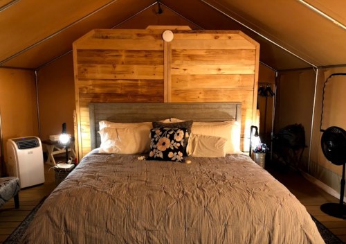 Cozy bedroom in a tent with a wooden accent wall, a large bed, and soft lighting.