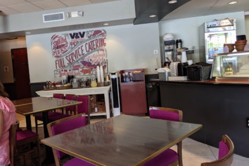 Interior of a café featuring tables with purple chairs, a service counter, and a wall mural about catering services.
