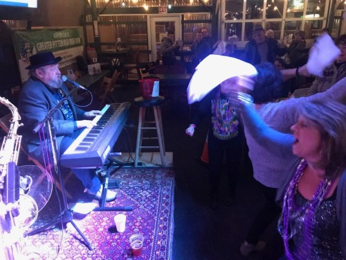 A lively scene with a pianist performing while people dance and enjoy the music in a festive atmosphere.