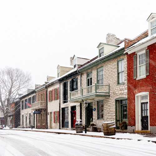 A snowy street lined with historic buildings, featuring stone and brick facades, and empty sidewalks.