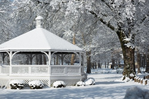 A snow-covered gazebo surrounded by trees blanketed in white, creating a serene winter landscape.