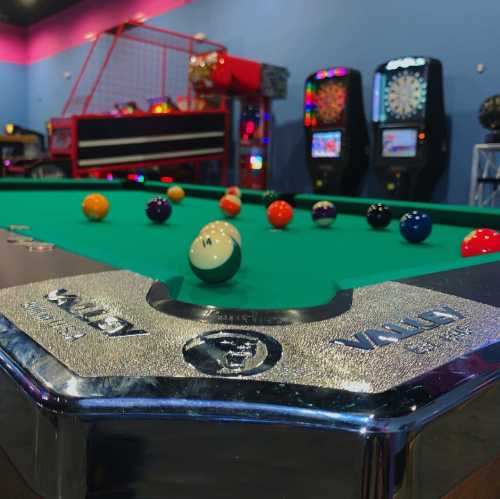 A pool table with colorful balls, set in a vibrant game room with arcade machines in the background.