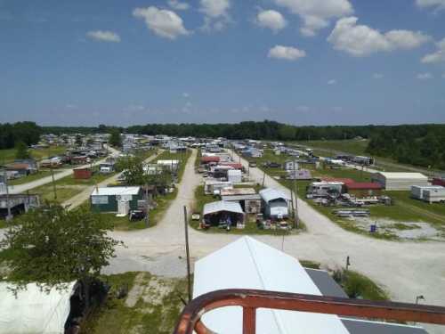 Aerial view of a large outdoor market with numerous stalls and vehicles under a blue sky with scattered clouds.