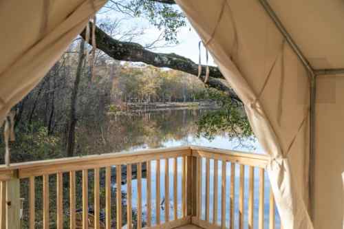 View from a tent overlooking a calm river surrounded by trees and autumn foliage.