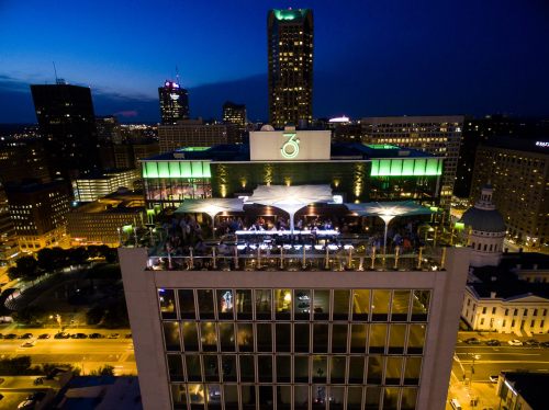 A rooftop bar illuminated at night, with city skyline views and people enjoying the atmosphere.