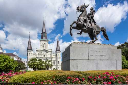 Statue of a horseman in front of a historic church with spires, surrounded by flowers and blue skies.