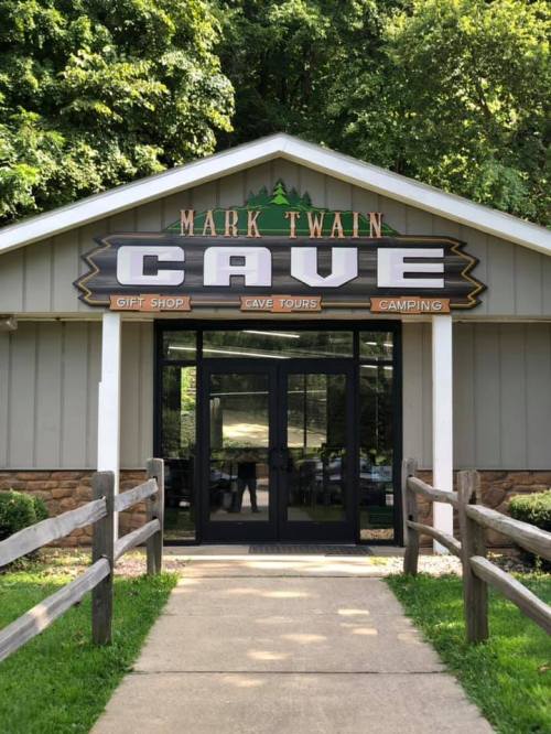 Entrance to Mark Twain Cave featuring a sign with "CAVE" and information about a gift shop, cave tours, and camping.