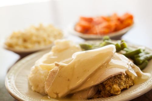 A plate of turkey with gravy, stuffing, mashed potatoes, green beans, and a side of carrots and rice.