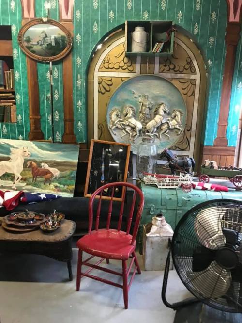 A vintage room with green wallpaper, antique furniture, horse paintings, and various collectibles displayed.