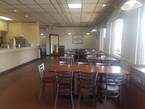 A spacious, empty restaurant with tables and chairs, a counter in the background, and large windows letting in light.