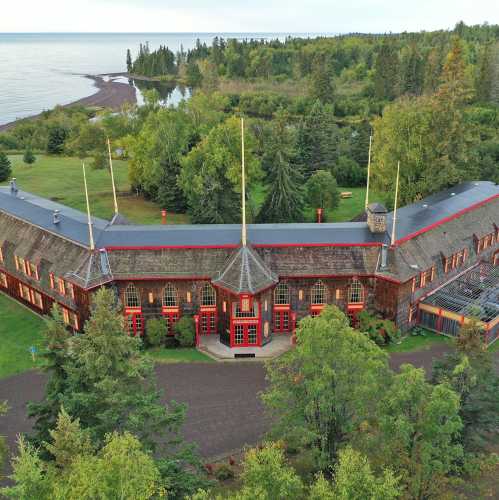 A scenic view of a large wooden building surrounded by trees, near a calm lake and shoreline.