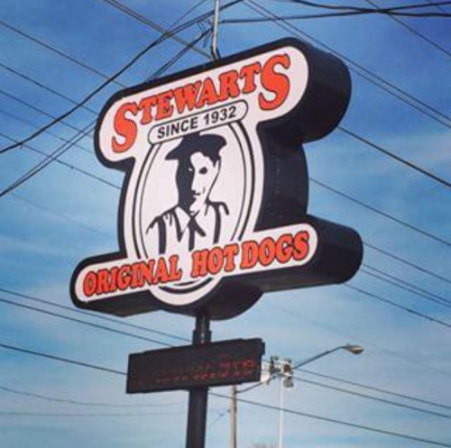Sign for Stewart's Original Hot Dogs, established in 1932, featuring a vintage design against a blue sky.
