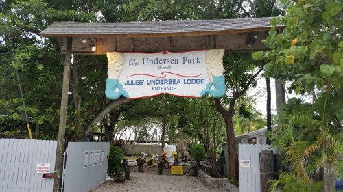 Entrance to Jules' Undersea Lodge at Key Largo Park, featuring a wooden sign and lush greenery.