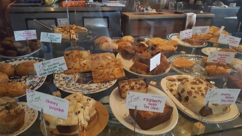 A display case filled with various baked goods, including pastries, cakes, and scones, each labeled with prices.