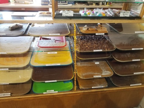A display case filled with various trays of colorful fudge and candy, labeled with different flavors.