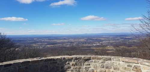 A panoramic view from a stone overlook, showcasing rolling hills and a clear blue sky with scattered clouds.