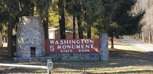 Sign for Washington Monument State Park, featuring stone pillars and surrounded by trees. Road visible in the background.