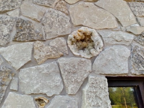 Close-up of a stone wall featuring a circular cavity filled with crystals, surrounded by rough, textured stones.
