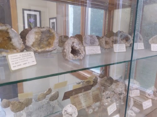 Display case filled with various geodes and mineral specimens, labeled with information about each piece.
