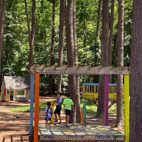 Children playing in a colorful outdoor playground surrounded by tall trees and nature.