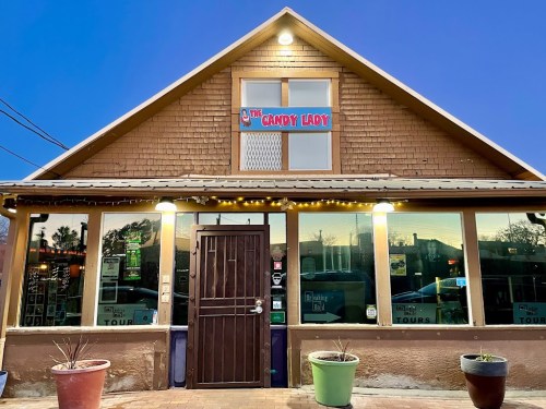 A cozy storefront of "The Candy Lady" with warm lights and a welcoming entrance at dusk.