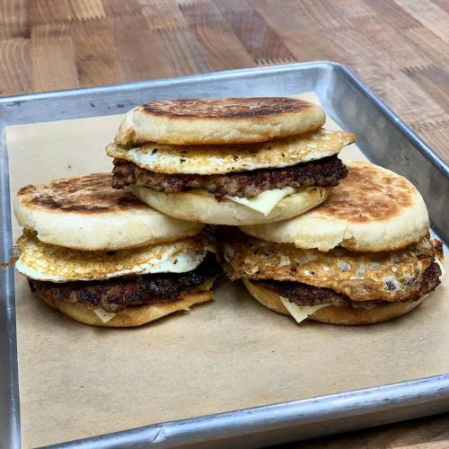 Three stacked breakfast sandwiches with crispy sausage, fried eggs, and melted cheese on toasted English muffins.