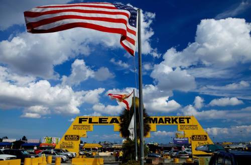 A vibrant flea market entrance with an American flag and a Florida flag under a blue sky with fluffy clouds.