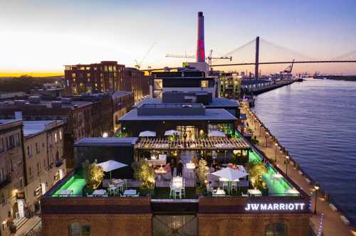 Aerial view of the JW Marriott with outdoor seating, overlooking a river at sunset, with city buildings in the background.