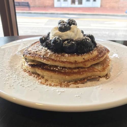 A stack of fluffy pancakes topped with whipped cream and fresh blueberries, dusted with powdered sugar.