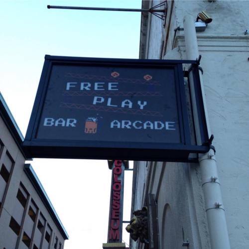 Sign outside a building reads "Free Play Bar Arcade" with a pixelated character graphic.