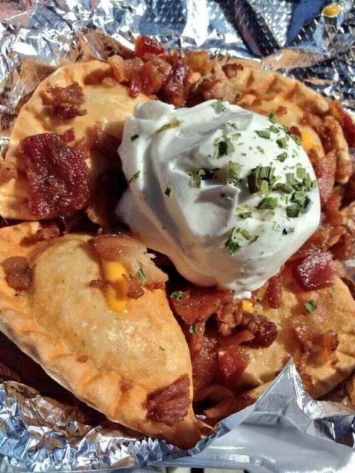 A close-up of a taco bowl filled with bacon, cheese, and topped with sour cream and herbs, served in foil.
