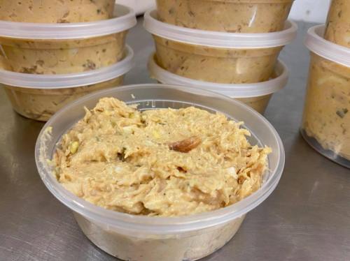 A clear container filled with a creamy, textured spread, surrounded by similar containers in the background.