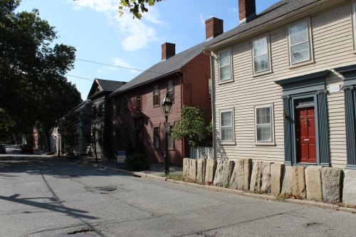 A quiet street lined with historic houses, featuring a mix of colors and stone barriers along the sidewalk.
