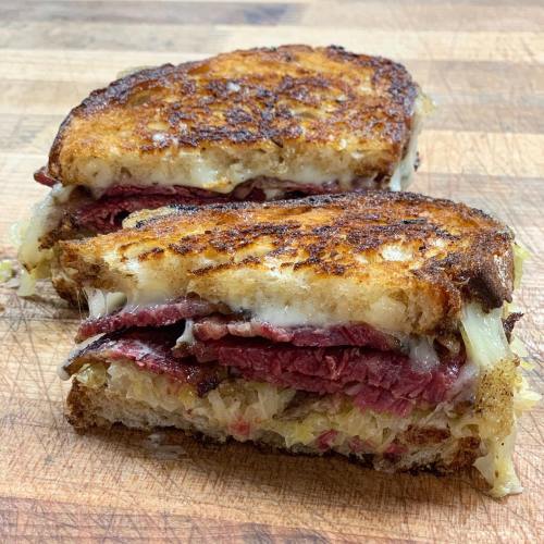 A close-up of a grilled sandwich with layers of corned beef and sauerkraut, toasted to a golden brown.