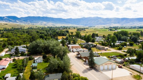 Aerial view of a small town surrounded by green fields and mountains under a partly cloudy sky.